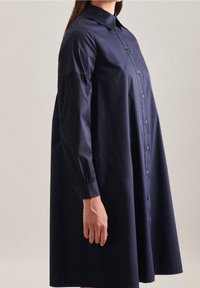 Tmavě modré košilové šaty vyrobené z bavlny. Mají klasický límeček, dlouhé rukávy s jemným prohnutím a délku ke kolenům.