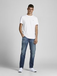 Camiseta blanca de algodón con un pequeño logo, combinada con vaqueros de mezclilla azules y zapatillas deportivas blancas. Conjunto casual simple sin patrones ni acentos.