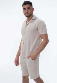 Chemise beige clair à manches courtes avec un col évasé et une fermeture à boutons, accompagnée de shorts assortis, fabriqués à partir d'un tissu texturé.