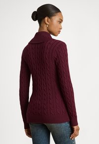 Vinrød kabelstrikket genser med oppbrettbar krage, ribbet kant og lange ermer, designet for en tettsittende silhuett.