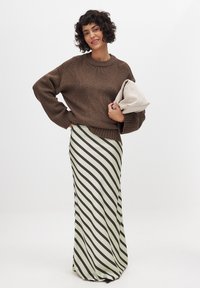 Brun strikket trøje med brede ærmer; gulvlængde nederdel i lys grøn med mørke diagonale striber; holder en lys clutch.