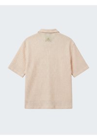 Chemise beige à manches courtes avec texture gaufrée et col, vue de dos avec une petite étiquette rectangulaire près de l'encolure.
