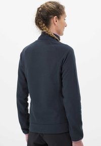 Chaqueta de forro polar azul marino con cuello alto, mangas raglán y puños de canalé. Textura suave y detalles cosidos en los hombros.