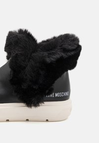 Svarta lädersneakers med en fluffig svart pälskrage, framhävda av vita "LOVE MOSCHINO"-logotypen på hälen och en strukturerad off-white sula.