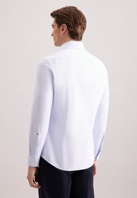 Camicia a maniche lunghe azzurro chiaro in morbido tessuto, con colletto classico e orlo curvo. Dettagli con bottoni sui polsini. Vestibilità su misura.