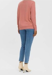 Hellrosa übergroßer Pullover kombiniert mit blauen, enganliegenden Jeans und beigen Knöchelstiefeln, mit einer weichen Textur und lässiger Silhouette.