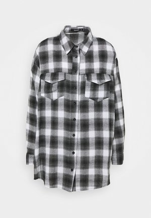 Chemise à carreaux noire et blanche à manches longues avec fermeture à boutons sur le devant et deux poches à rabat sur la poitrine, style décontracté.