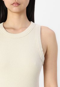 Ermeløs, ribbet tanktopp i off-white. Har en rund halslinning og teksturert stoff. Designet fremhever en tettsittende fasong.