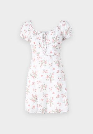 Balta gėlių suknelė su trumpomis pūkuotomis rankovėmis, turinti raištelių priekį ir prigludusį liemenį, puošta rožinėmis ir žaliomis gėlių raštais.