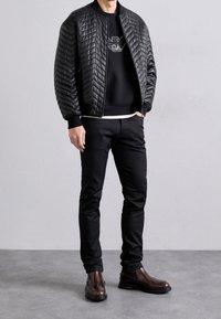 Black quilted bomber jacket with ribbed cuffs, worn over a black sweatshirt. Paired with black pants and brown leather boots.