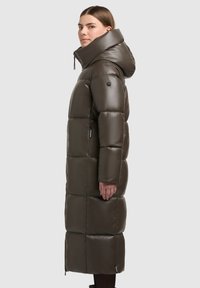 Parka lung, pufos, în verde oliv închis. Fabricat dintr-un material lucios și neted, cu guler înalt și glugă mare. Prezintă secțiuni matlasate și buzunare.