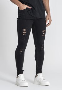 Mustat farkkuleggarit, joissa on repimiä ja joustavaa materiaalia. Parina valkoiset lenkkarit kontrastia varten.