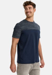 Marineblaue T-Shirt mit einem strukturierten grauen Oberpaneel, kurzen Ärmeln, Rundhalsausschnitt und einer kleinen Brusttasche. Baumwollmischung.