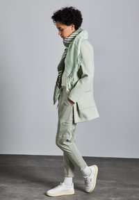 Hellgrüner, übergroßer Mantel, lässige Cargo-Hosen, weiße Sneakers und ein gestreifter Minzschal mit Fransen. Glatte Stoffe und lässiges Design.