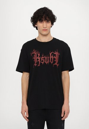 T-shirt nera in cotone con maniche corte, caratterizzata da una grande scritta in stile fiamma rossa "KsuH!" centrata sulla parte anteriore. Design semplice, vestibilità rilassata.