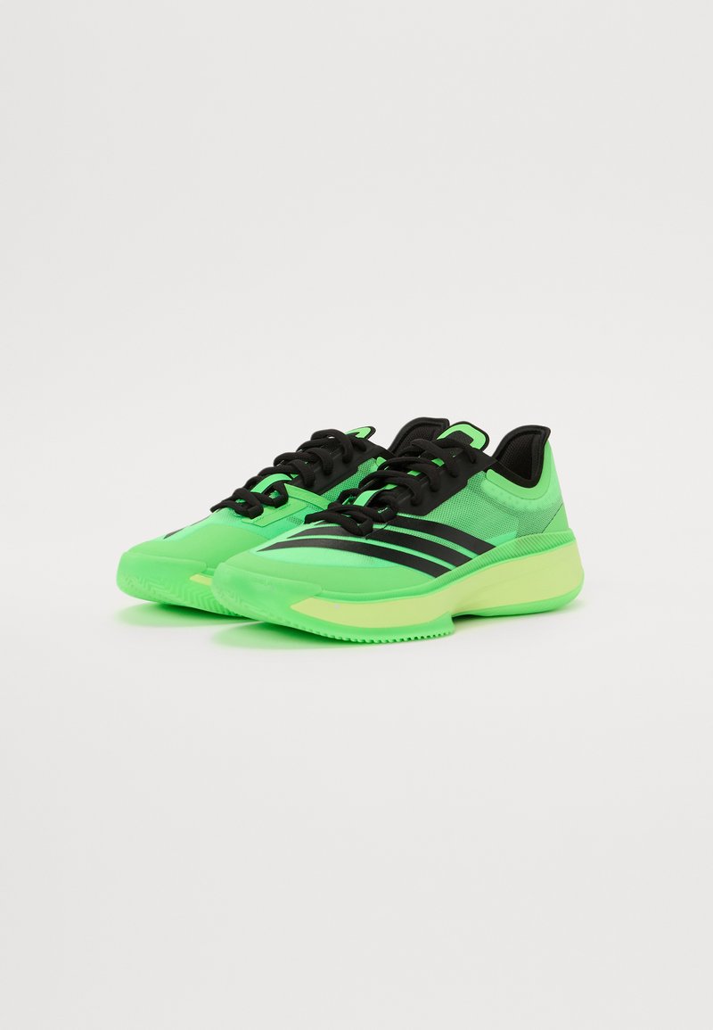 Zapatillas deportivas de color verde neón con acentos negros, que presentan una parte superior de malla, un sistema de cierre con cordones en el frente y una suela texturizada para mayor tracción.