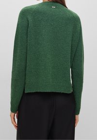 Green knitted sweater with a rounded neckline and a slightly cropped fit. Features ribbed cuffs and hem. Brand logo is located at the back.