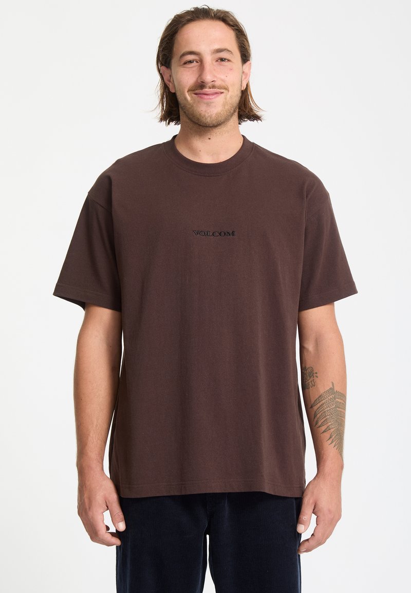 T-shirt marron à manches courtes en coton avec un col rond, arborant un logo "VOLCOM" noir brodé sur la poitrine.