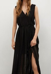 Robe maxi noire avec un décolleté en V, sans manches, taille cintrée par une ceinture en corde, avec un tissu transparent à rayures verticales et une fente latérale.