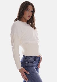 Maglione bianco corto con corpo testurizzato e maniche a coste, abbinato a jeans blu con dettaglio della tasca posteriore.