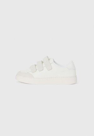 Zapatilla blanca con parte superior de cuero liso, tres correas de Velcro en el empeine, puntera redondeada y una suela de goma gruesa de color claro.