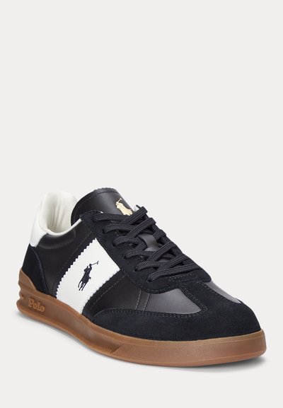 Men's sneaker featuring a combination of black leather and suede with white accents, a rubber sole, and gold logo detail.