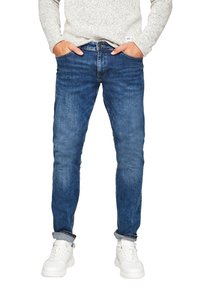 Blue denim jeans with a slim fit, featuring a faded wash, five-pocket design, and rolled cuffs, paired with white sneakers.