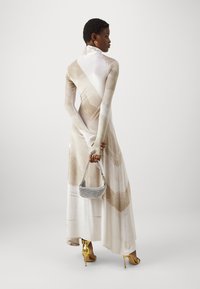 Lang, aansluitend jurkje van zachte beige en witte stof met abstracte patronen; gecombineerd met een kleine metallic handtas en gele hoge hakken.