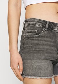 Shorts en denim gris avec un ourlet éfrangé, dotés d'un design classique à cinq poches, de passants de ceinture cousus et d'une texture douce.