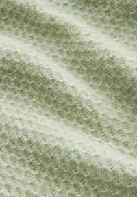Gros plan sur un tissu doux et texturé avec un motif en maille gaufrée de couleur vert pâle, montrant de fines fibres et de subtils ombres sur les plis.