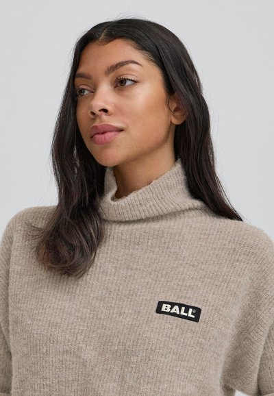 Beige pletený svetr s rolákem, na přední straně s černým obdélníkovým štítkem s nápisem "BALL". Měkká, texturovaná tkanina.