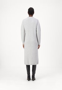 Robe grise à manches longues en tissu tricoté doux, avec une coupe droite, des poignets côtelés et une longueur mi-mollet, associée à des bottes à talons hauts noires.