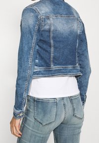 Jeansjacka i medelblått med en kort design, som har kontrasterande sömmar, knäppta muddarna och en avslappnad passform. Matchas med ljus tvättade jeans.