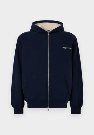 Sudadera con cremallera de color navy en una suave mezcla de algodón, con interior forrado, bolsillos delanteros y logo bordado en el lado izquierdo del pecho. Capucha con cordón ajustable.