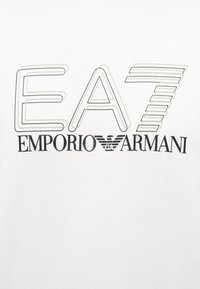 Λογότυπο EA7 με στυλιζαρισμένα γράμματα πάνω από το κείμενο «EMPORIO ARMANI» και το έμβλημα του αετού Armani στο κέντρο σε λευκό φόντο.