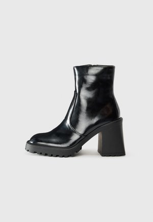 Bottine en cuir noir avec un talon bloc haut, semelle texturée, embout arrondi et détail de fermeture éclair sur le côté.