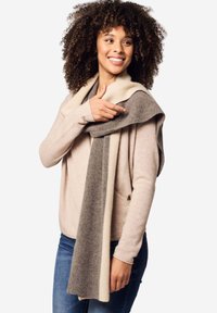 Maglione a maglia e sciarpa in tonalità neutre. La sciarpa presenta un design a gradiente con righe crema e grigie. Il modello mostra il suo stile a strati.