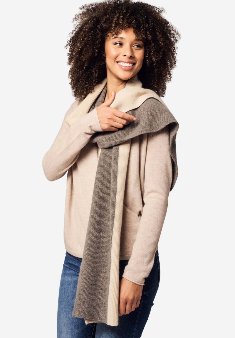 Maglione a maglia e sciarpa in tonalità neutre. La sciarpa presenta un design a gradiente con righe crema e grigie. Il modello mostra il suo stile a strati.
