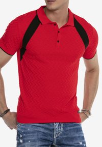 Rotes Polohemd mit einem strukturierten Zickzackmuster, schwarzen Seitenpaneelen, kurzen Ärmeln und einem klassischen Kragen mit zwei Knöpfen.