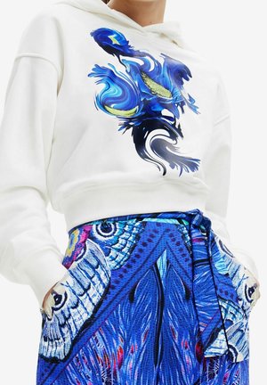 Sweat à capuche blanc avec un design abstrait en tourbillons bleus et verts, associé à une jupe bleue à motifs avec des motifs d'ailes de papillon et une ceinture nouée à la taille.