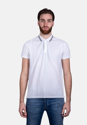 Polo shirt bianco a maniche corte, con colletto a righe a contrasto e patta con bottoni. Indossato con jeans in denim blu.