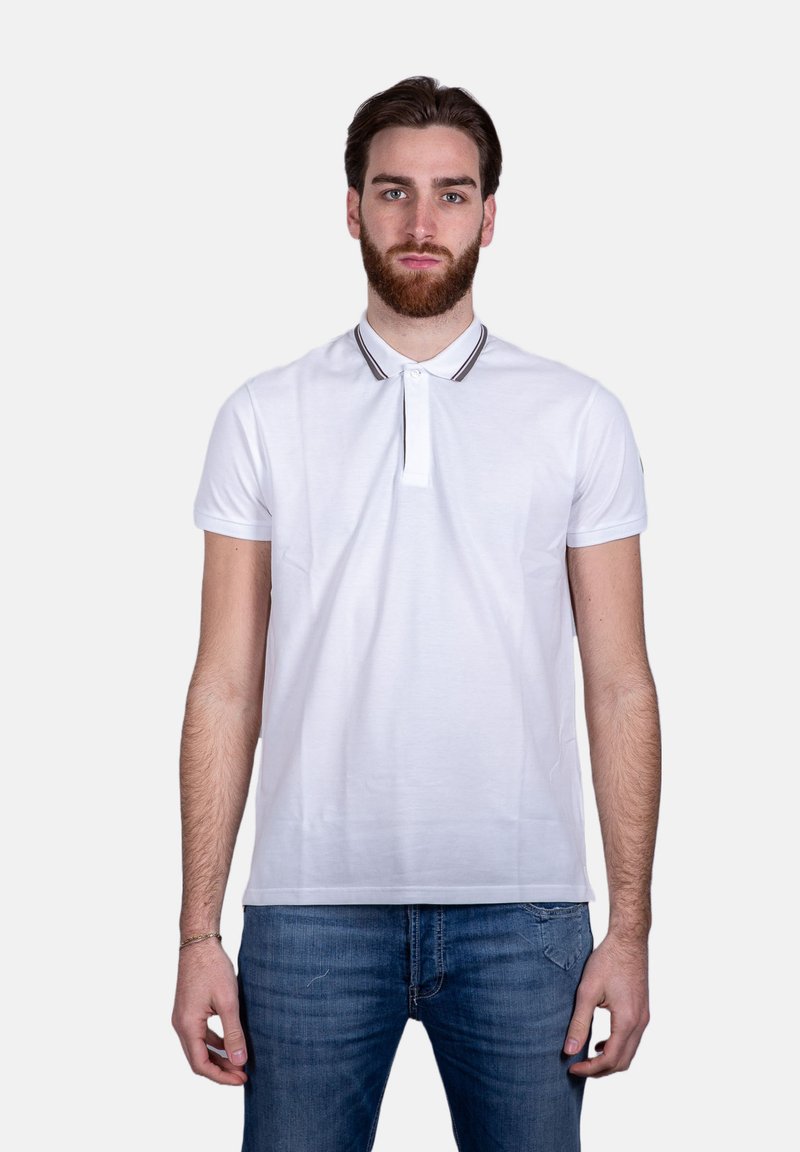 Polo shirt bianco a maniche corte, con colletto a righe a contrasto e patta con bottoni. Indossato con jeans in denim blu.