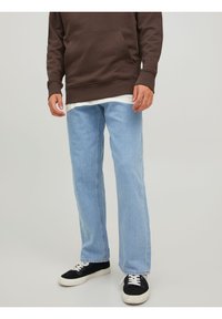 Jean en denim bleu clair avec une coupe droite, associés à un sweat à capuche marron foncé et des baskets noires. Le sweat à capuche a une poche frontale.