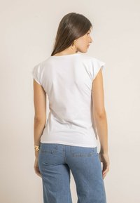 Haut blanc à manches courtes avec une coupe décontractée, présentant des manches retroussées et une texture lisse. Porté avec un jean bleu à jambes larges.