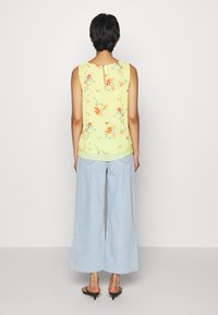 Top de tirantes floral amarillo con detalle de abertura en la espalda, combinado con unos jeans de pierna ancha de color azul claro. El top presenta una tela suave y ligera.