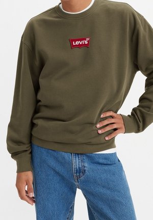 Sudadera de color verde oliva con escote redondo y corte relajado. Presenta un logo de Levi's bordado en rojo y puños acanalados. Combinada con vaqueros azules.