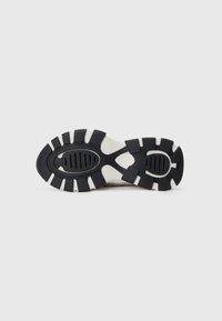 Sort og hvid sneakersål med et tekstureret design, der har fremtrædende dæksler og ovale udskæringer, som giver godt greb og støtte.