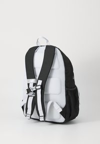 Mochila em preto e branco com textura em malha acolchoada; possui alças ajustáveis, fecho de fivela segura e um bolso lateral para armazenamento.