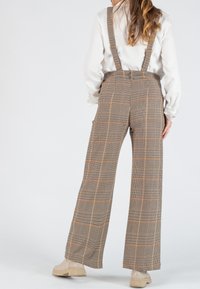 Pantalon à bretelles à carreaux bruns avec une coupe large. Présente un motif à carreaux avec des touches d'orange et une taille haute. Texture de tissu lisse.