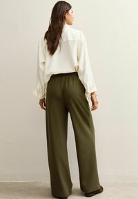 Romige blouse met losse pasvorm en omgeslagen mouwen, gecombineerd met olijfgroene wijde broek met een elastische tailleband. Textuur achtergrond.